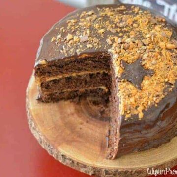 A chocolate cake, with a large wedge cut out, resting on a rustic, wood cutting