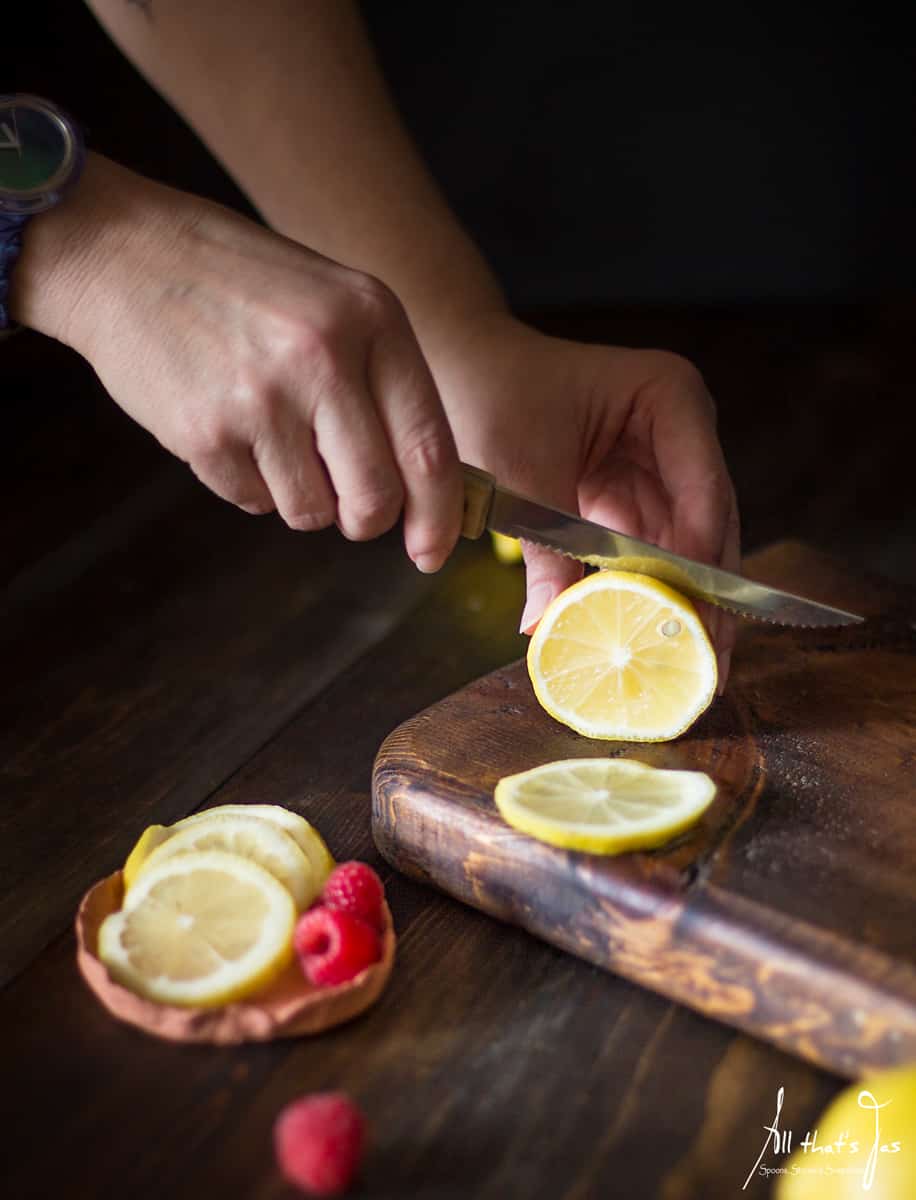A person cutting slices of lemon on a wooden cutting board