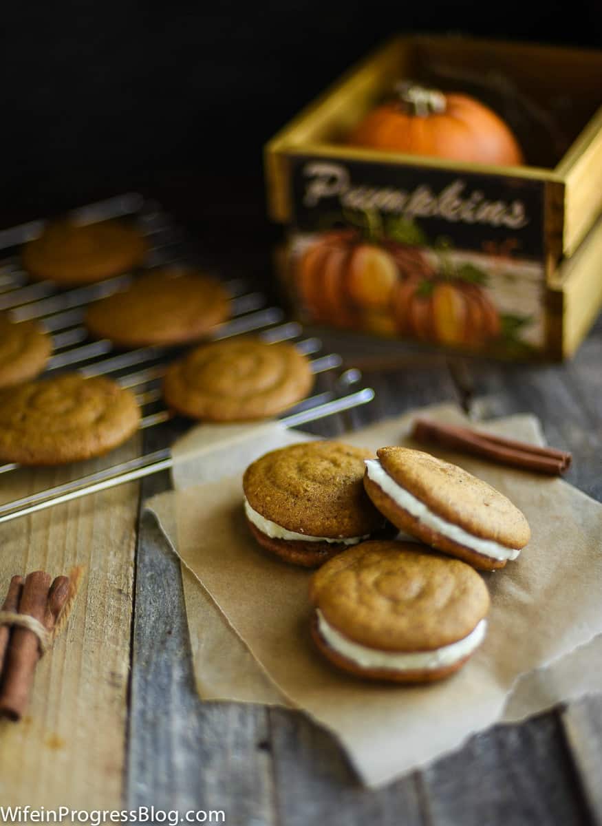 Pumpkin whoopie pies with cream cheese filling with more resting on a wire rack