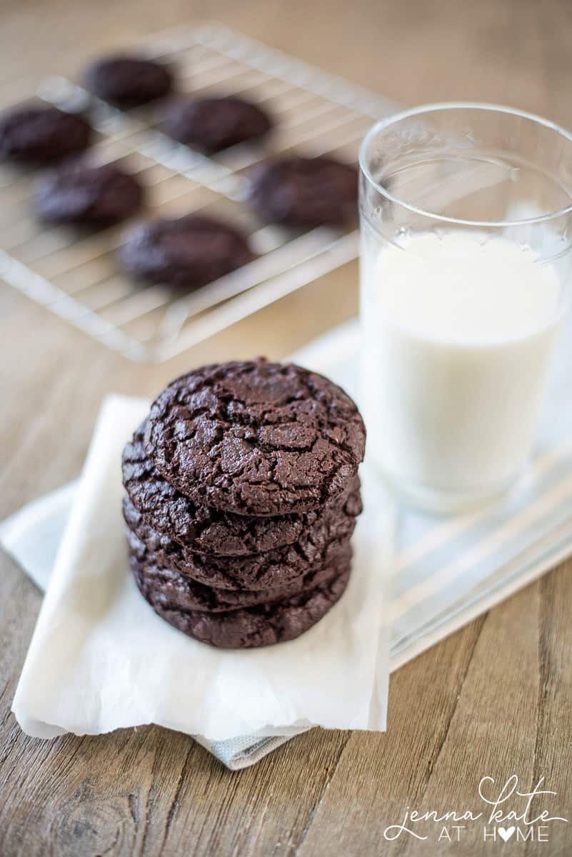 A stack of chocolate cookies on a napkin, near  a glass of milk