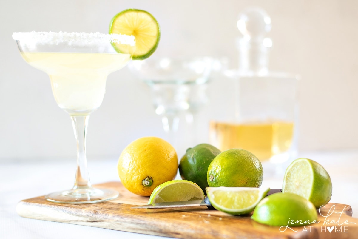 Cutting board with limes, lemons and a glass of homemade margarita mix