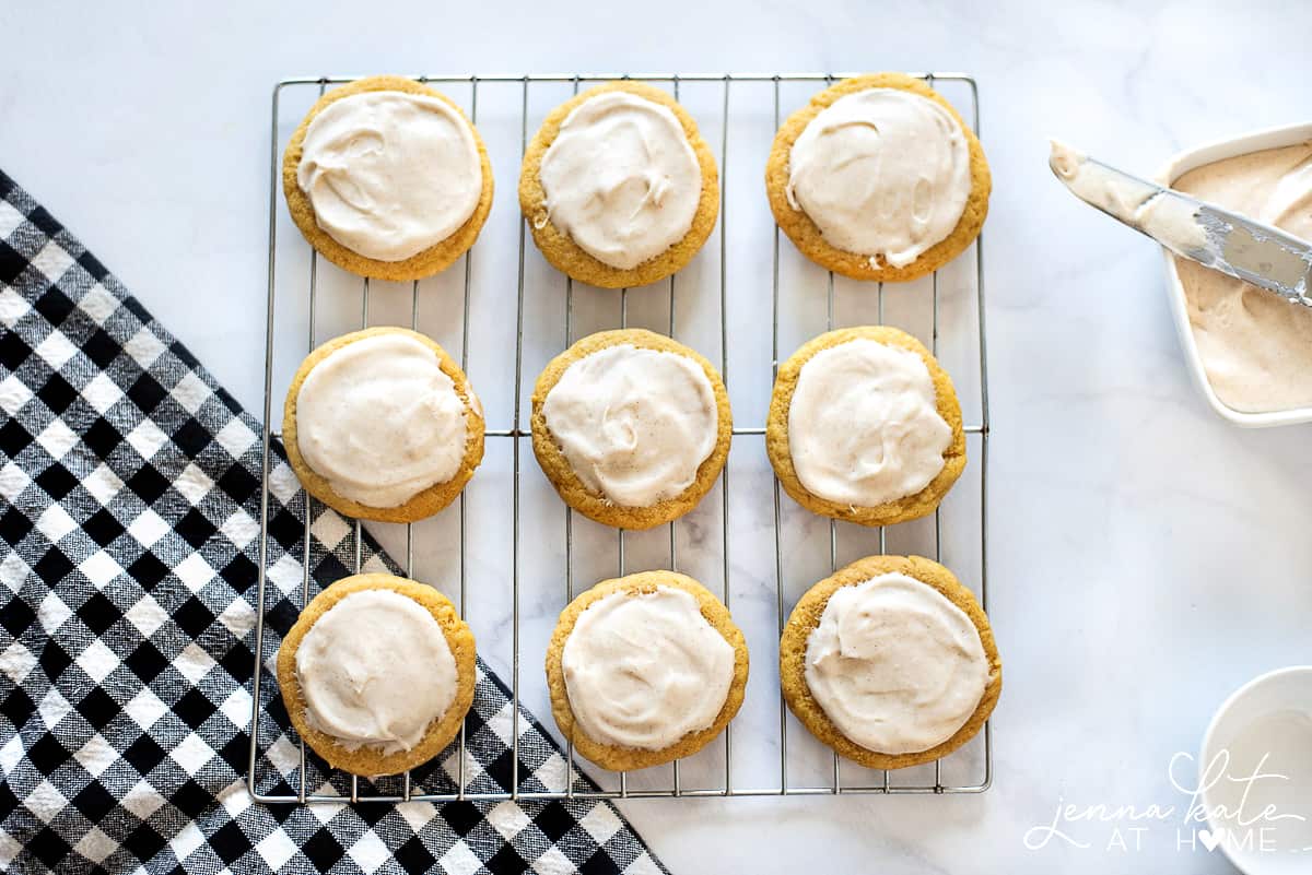 Pumpkin sugar cookies with cinnamon cream cheese frosting, resting on wire cooling rack