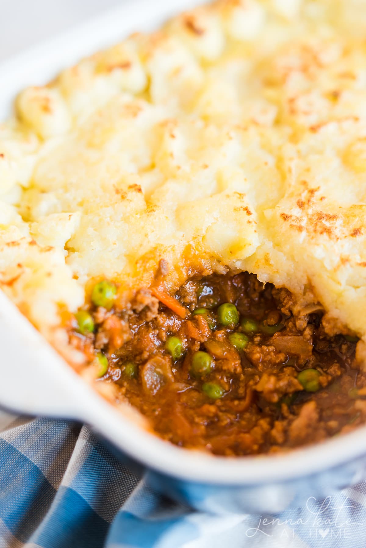 Close up of the meat filling in the shepherd's pie. Potato on top with sauce, ground beef, carrots and peas visible below.
