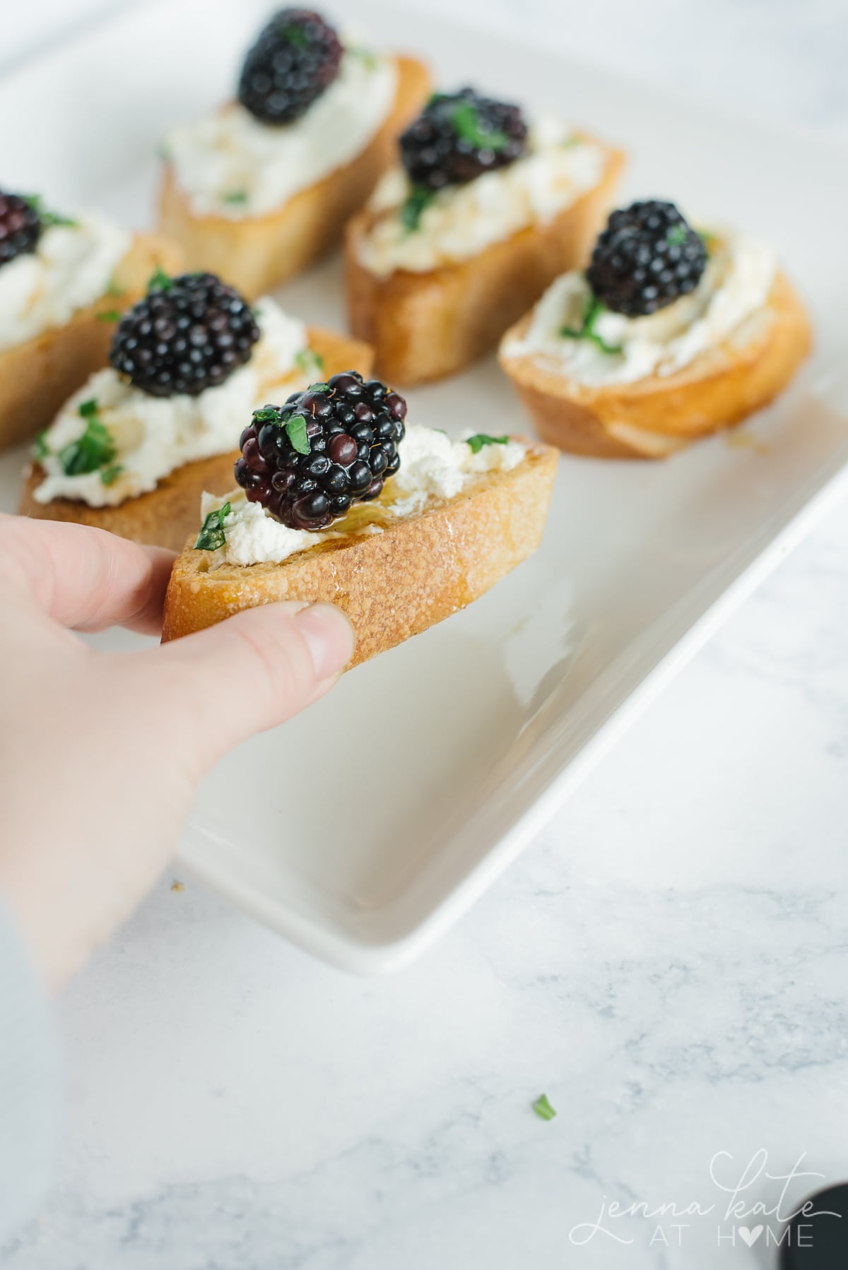 Hand picking up one of the blackberry and goat cheese crostini appetizers