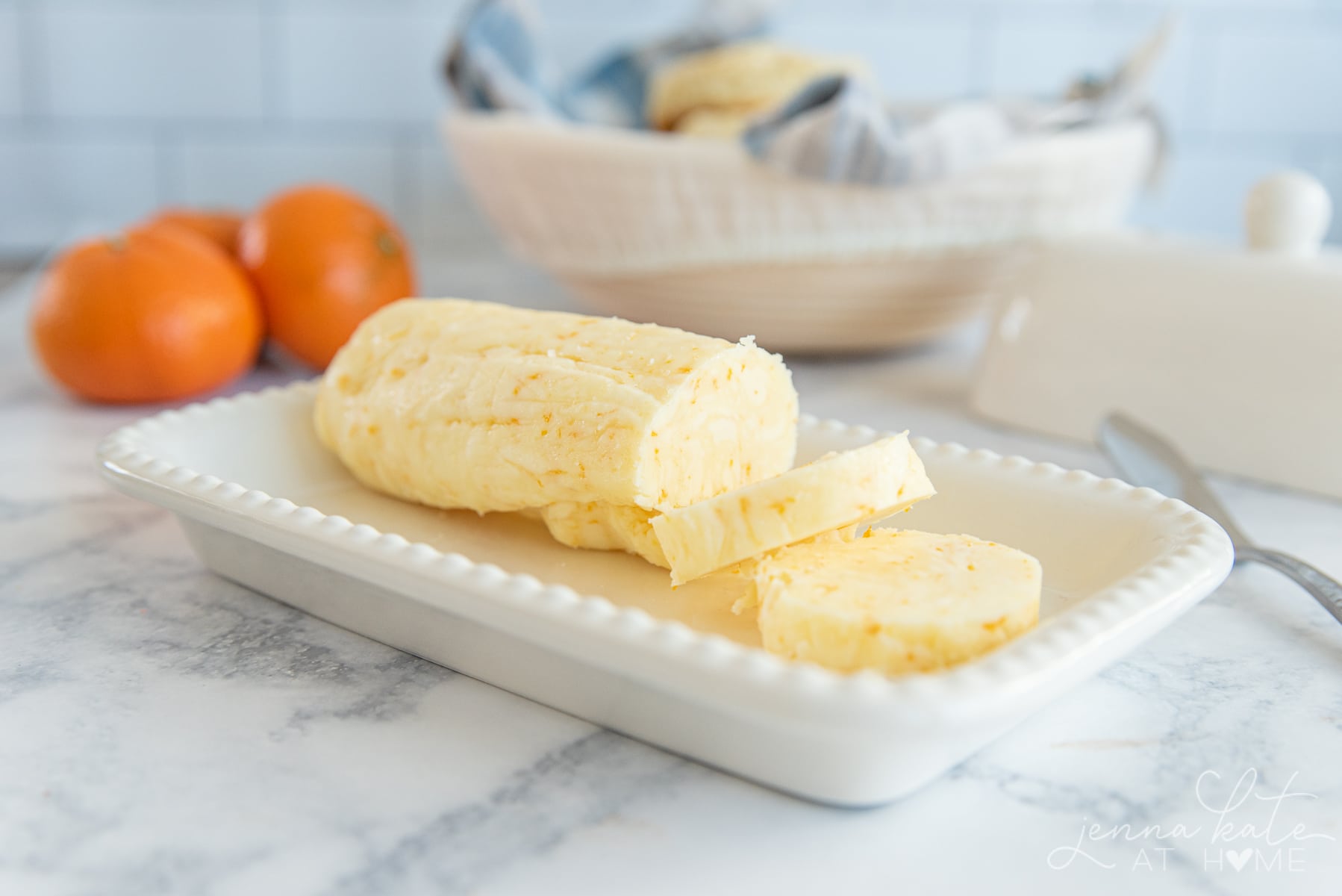 log of orange butter with 2 cut slices and an oranges in the background