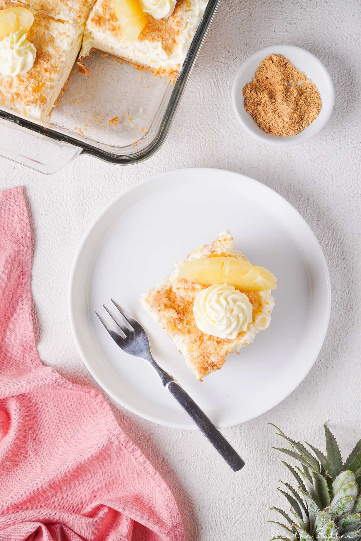 Slice of pineapple cream pie on a white plate next to a pink napkin.